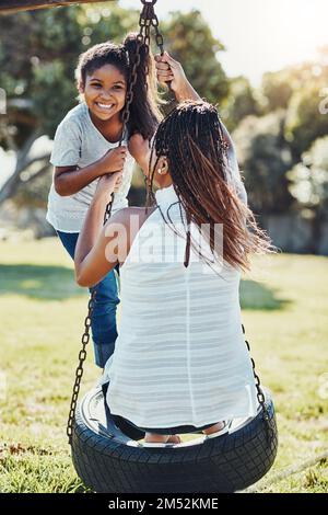 Das wird ein Tag voller Spaß. Eine Mutter schubst ihre Tochter auf eine Schaukel im Park. Stockfoto