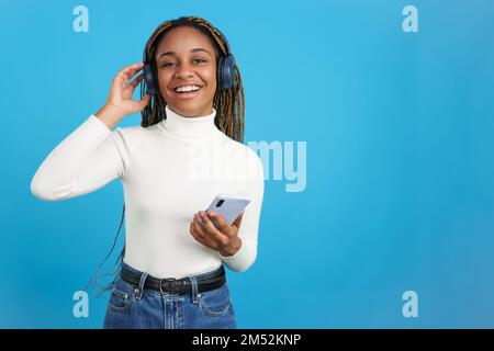 Lächelnde afrikanische Frau, die in die Kamera schaut, während sie Musik hört Stockfoto