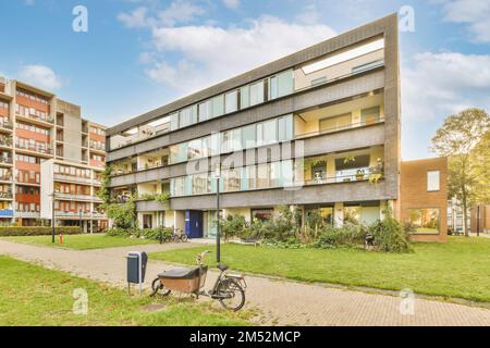 Ein Apartmentkomplex in der Stadt mit Fahrrädern, die auf dem Bürgersteig geparkt sind und Bäume entlang der Seite des Gebäudes wachsen Stockfoto