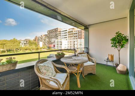 Ein Balkon mit Stühlen, Tischen und einer Pflanze auf dem Rasen vor den Fenstern des Apartments Stockfoto