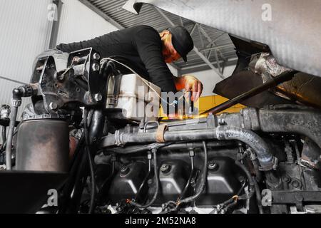 Automechaniker repariert großen Lkw oder Traktor in der Werkstatt. Professioneller Mechaniker repariert Lkw-Motor. Aufrichtiger Arbeiter. Stockfoto