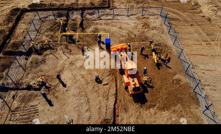 Bagger mit Luftaufnahme und Bauarbeiter, die auf der Baustelle im Freien arbeiten. Rohrverlegung im Graben zur Vergasung. Top-Punkt der Aufnahme. Reparatur und Wiederherstellung der Erdgasversorgung. Stockfoto