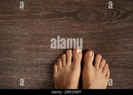 Weibliche Beine ohne Schuhe auf braunem Holzboden, Ansicht von oben nach unten Stockfoto