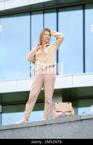 Eine sportliche Frau mittleren Alters blickt in die Ferne und glättet ihr windgeblasenes Haar Stockfoto