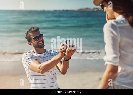 Ich wähle dich, jeden einzelnen Tag meines Lebens. Ein junger Mann, der seiner Freundin an einem Sommertag am Strand einen Heiratsantrag macht. Stockfoto