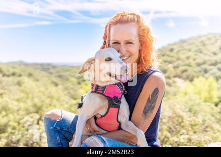 Eine Frau umarmt einen Hund, während sie auf dem Berg sitzt Stockfoto