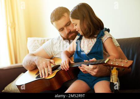 An dem Tag, an dem sie beschloss, Gitarrist zu werden. Ein bezauberndes kleines Mädchen, das mit ihrem Vater zu Hause Gitarre spielt. Stockfoto