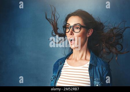Wer hat die Klimaanlage eingeschaltet? Studiofoto einer jungen Frau, die vor blauem Hintergrund Luft ins Gesicht geblasen hat. Stockfoto