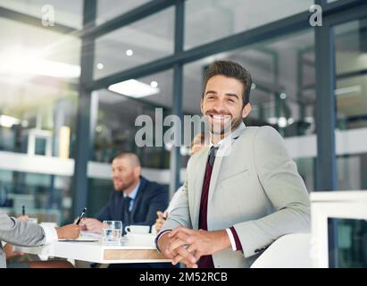 Er ist ein selbstbewusster Gamer. Porträt eines Geschäftsmannes, der im Büro mit seinen Kollegen im Hintergrund sitzt. Stockfoto