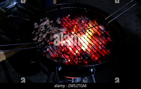 Fleisch wird abends bei Grillveranstaltungen auf Kohlen gekocht. Stockfoto