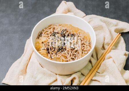 Koreanische Küche Naengmemilguksu, eine winterliche Delikatesse, wird dieses Buchweizen-Nudelgericht in einer kalten Hühnchen- oder Rinderbrühe serviert und mit einer kalten Scheibe garniert Stockfoto