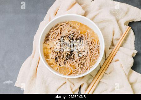 Koreanische Küche Naengmemilguksu, eine winterliche Delikatesse, wird dieses Buchweizen-Nudelgericht in einer kalten Hühnchen- oder Rinderbrühe serviert und mit einer kalten Scheibe garniert Stockfoto