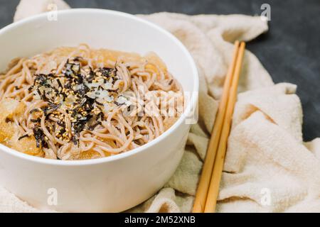 Koreanische Küche Naengmemilguksu, eine winterliche Delikatesse, wird dieses Buchweizen-Nudelgericht in einer kalten Hühnchen- oder Rinderbrühe serviert und mit einer kalten Scheibe garniert Stockfoto