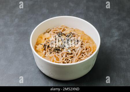 Koreanische Küche Naengmemilguksu, eine winterliche Delikatesse, wird dieses Buchweizen-Nudelgericht in einer kalten Hühnchen- oder Rinderbrühe serviert und mit einer kalten Scheibe garniert Stockfoto