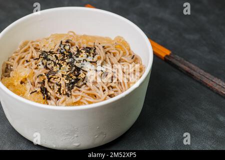 Koreanische Küche Naengmemilguksu, eine winterliche Delikatesse, wird dieses Buchweizen-Nudelgericht in einer kalten Hühnchen- oder Rinderbrühe serviert und mit einer kalten Scheibe garniert Stockfoto