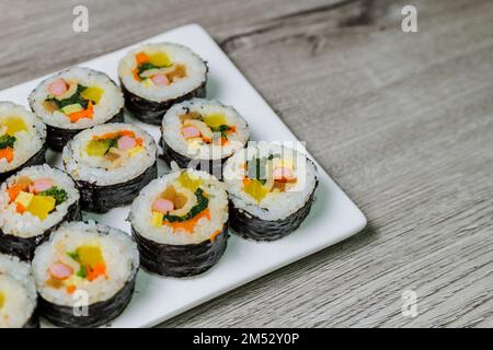 Reis mit Salz und Sesamöl gewürzt und in ein Blatt gerösteten gim (getrockneter Lava) mit Spinat, Karotten und eingelegtem weißem Rettich gerollt. Der lange Stockfoto