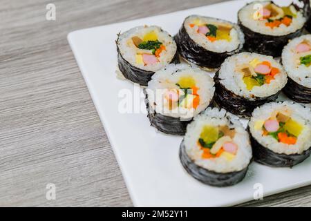 Reis mit Salz und Sesamöl gewürzt und in ein Blatt gerösteten gim (getrockneter Lava) mit Spinat, Karotten und eingelegtem weißem Rettich gerollt. Der lange Stockfoto