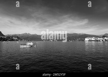 Kleine Holzboote am Lago Maggiore in Stresa, Landschaften über dem See im Hintergrund der alpen, schwarz weiß Stockfoto