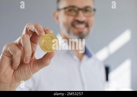 Nahaufnahme einer Münze mit einem Bitcoin-Symbol in der Hand eines glücklichen Geschäftsmannes Stockfoto