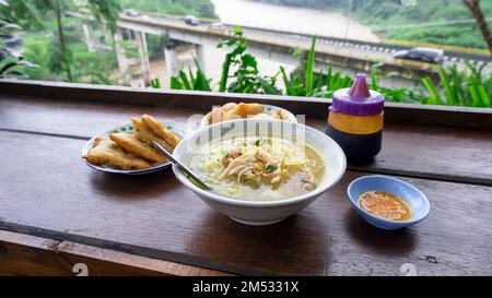 Indonesische traditionelle Küche namens soto mit Blick auf Brücken und Flüsse vor der Kulisse von grünen Bäumen, Hügeln und Bergen Stockfoto