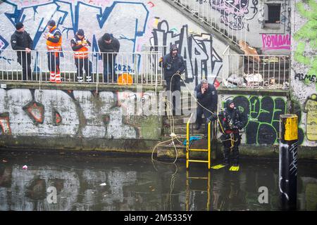 Berlin, Deutschland. 25. Dezember 2022. Polizeitaucher werden während einer Durchsuchung des Landwehrkanals vom Notfallpersonal beobachtet. Die Suche nach Beweisen im Fall des spektakulären Juwelendiebstahls aus dem Grünen Gewölbe in Dresden geht an Weihnachten weiter. Nach Angaben der Dresdner Polizei suchen am Sonntag seit den Morgenstunden rund 20 Polizeitaucher aus verschiedenen Staaten im Landwehrkanal am Kiehlufer im Bezirk Neukölln nach Beweisstücken. Kredit: Christophe Gateau/dpa/Alamy Live News Stockfoto