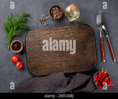 Hintergrund mit dunklem Schneidebrett, Öl, Sauce, Gewürzen, Kräutern und Chili-Paprika auf dunklem Küchentisch. Draufsicht und Kopierbereich. Stockfoto
