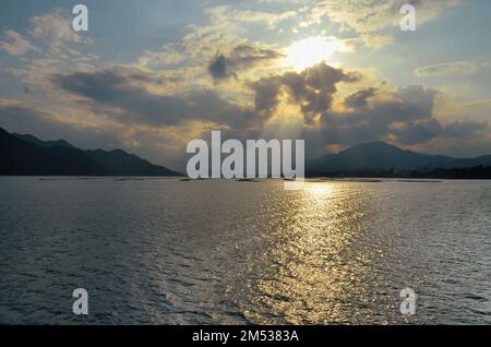 Sonnenuntergang in der Bucht von Hiroshima, Seto-Binnensee, zwischen der Insel Itsukushima und der Stadt Hatsukaichi. Präfektur Hiroshima, Japan. Stockfoto