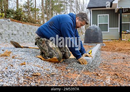 Mit einem professionellen Deckenfertiger legt er Steine für das Pflasterprojekt ab. Stockfoto