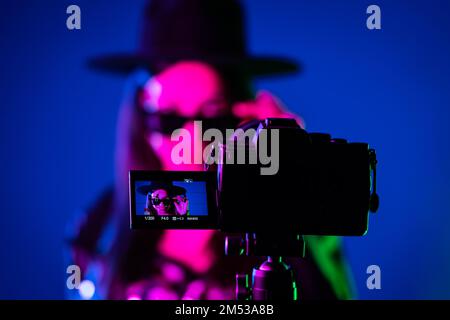 Backstage wie ein Bediener mit einer professionellen Kamera arbeitet. Der Videofilmer nimmt mit einer Schauspielerin oder Sängerin in einem Dark Studio einen Musikclip auf Stockfoto