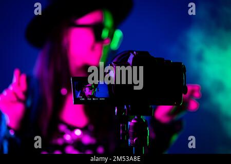 Backstage wie ein Bediener mit einer professionellen Kamera arbeitet. Der Videofilmer nimmt mit einer Schauspielerin oder Sängerin in einem Dark Studio einen Musikclip auf Stockfoto