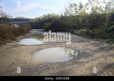Unbefestigter Pfad mit Pfützen und einer Brücke im Hintergrund auf dem Land Stockfoto