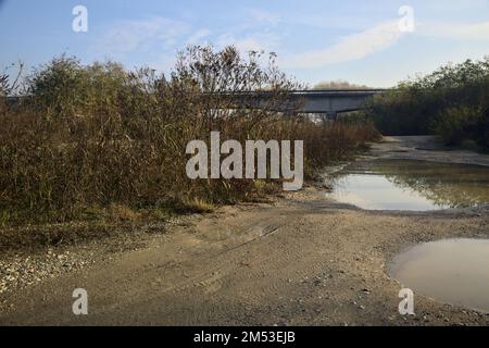 Unbefestigter Pfad mit Pfützen und einer Brücke im Hintergrund auf dem Land Stockfoto