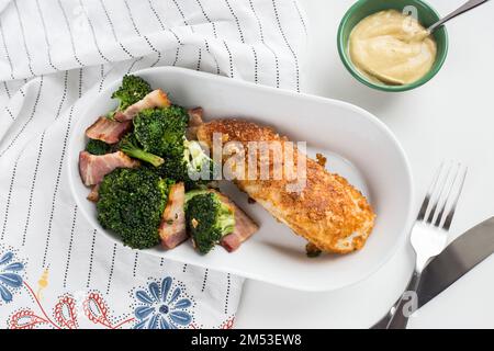 Ein Blick von oben auf das Huhn mit Brokkoli und Fleischscheiben auf einer weißen Schüssel mit einer Gabel und einem Messer neben einer gelben Sauce Stockfoto