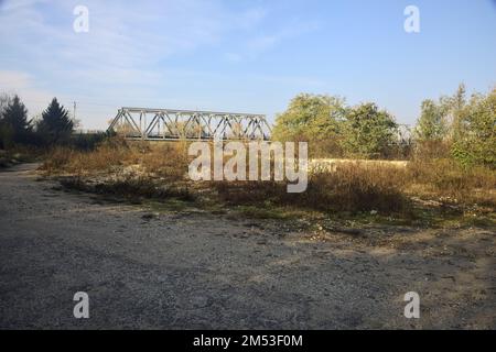 Unbefestigter Pfad mit Pfützen und einer Brücke im Hintergrund auf dem Land Stockfoto