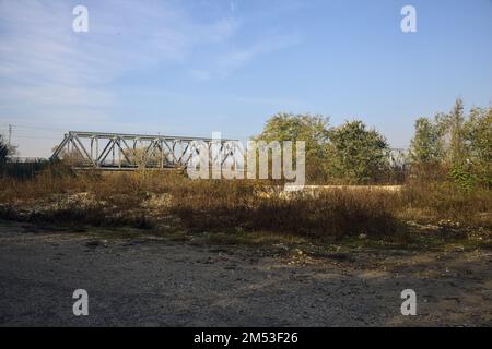 Unbefestigter Pfad mit Pfützen und einer Brücke im Hintergrund auf dem Land Stockfoto