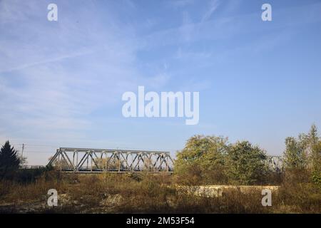 Unbefestigter Pfad mit Pfützen und einer Brücke im Hintergrund auf dem Land Stockfoto