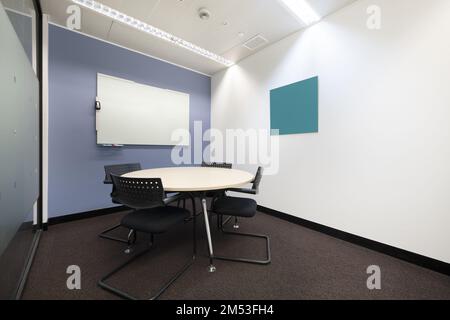 Sitzungssaal mit rundem weißen Holztisch mit schwarzen Stühlen und Whiteboard mit Deleble-Markern Stockfoto