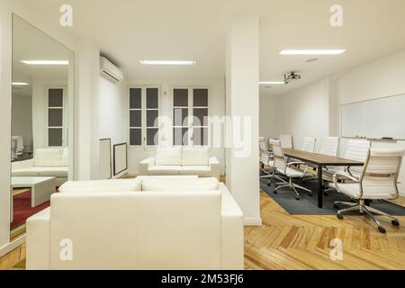Büro mit weißen Ledersofas, Hartholzfußboden und Konferenztisch mit weißen Drehstühlen Stockfoto