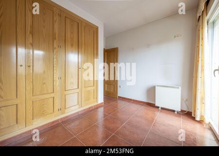 Schlafzimmer mit einem vierteiligen eingebauten Kleiderschrank mit Eichentüren, glänzend braunem Steinzeug-Fußboden und elektrischem Heizspeicher Stockfoto