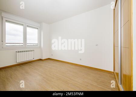 Schlafzimmer mit einem vierteiligen eingebauten Kleiderschrank mit Eichentüren, glänzend braunem Steinzeug-Fußboden und elektrischem Heizspeicher Stockfoto