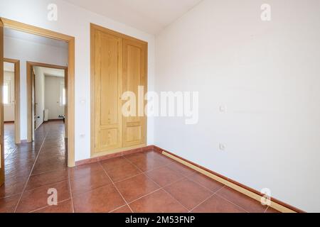 Schlafzimmer mit einem zweiteiligen eingebauten Kleiderschrank mit Eichentüren und rötlich-braunem Steinzeug-Boden und Zugang zu einem Verteiler Stockfoto