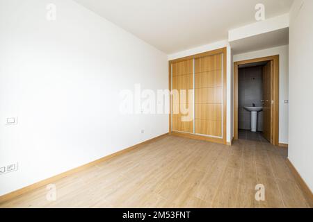 Schlafzimmer mit zweiteiligem eingebautem Kleiderschrank mit Schiebetüren aus Eichenholz, Holzfußboden aus Steinzeug und Zugang zu einem eigenen Badezimmer Stockfoto