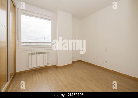 Schlafzimmer mit zweiteiligem eingebautem Kleiderschrank mit großen Schiebetüren aus Eichenholz und Holzfußboden, einteiligem Aluminiumfenster mit Aussicht und Aluminium Stockfoto