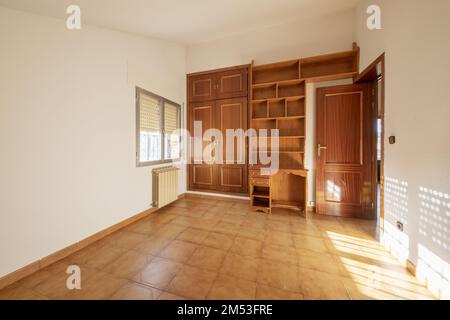 Schlafzimmer mit eingebautem Schrank mit Sapelly-Falttüren, Fußleisten und Innentüren aus demselben Material und hellbraunem Steinzeug-Boden Stockfoto