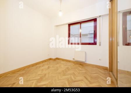 Leeres Schlafzimmer mit dunkelrot eloxierten Aluminiumfenstern, Parkettfußboden aus französischer Eiche und eingebautem Kleiderschrank mit Spiegelschiebetüren Stockfoto