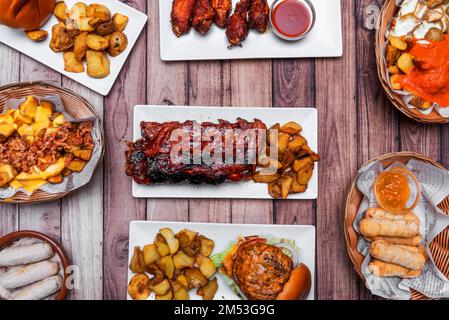 Set aus Fast-Food-Gerichten mit Schweinerippchen mit Kartoffeln, gemischten Hamburgern, tequeños gefüllt mit Käse, pommes frites mit Käse und Speck Stockfoto