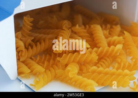 Glutenfreie Fusilli-Pasta aus Mais und Reis, die aus einer Schachtel ausläuft. Schließen. Stockfoto