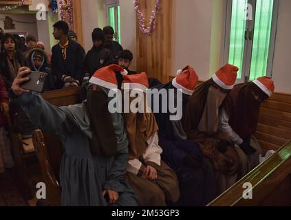 Kaschmirisch verschleierte muslimische Frauen machen ein Selfie, wenn sie an der Weihnachtsmesse mit Christen in der katholischen Kirche der Heiligen Familie teilnehmen, während Christen an der Weihnachtsmesse in der katholischen Kirche der Heiligen Familie am 25. Dezember 2022 in Srinagar, der Sommerhauptstadt des von Indien verwalteten Kaschmir, teilnehmen. Die umstrittene Region des Himalaya in Kaschmir hat eine winzige Bevölkerung von Christen, von denen Hunderte an Weihnachten in der katholischen Kirche der Heiligen Familie zur Messe gehen und für Frieden und Wohlstand in der Region beten. (Foto: Mubashir Hassan/Pacific Press) Stockfoto