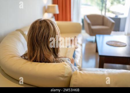 Eine Frau auf dem Rücken, die auf dem Sofa ihrer Wohnung auf entspannte und friedliche Weise liegt. Stockfoto