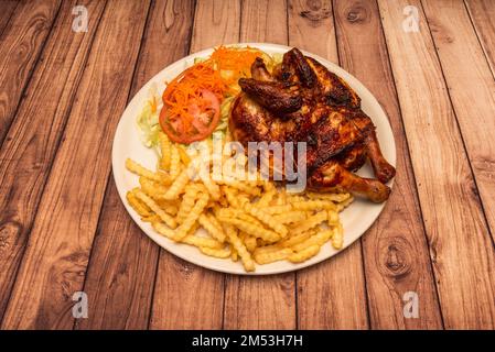 Ein gebratenes Hähnchen mit goldener Haut, dazu viele Pommes Frites und einen Salat und Tomatensalat Stockfoto